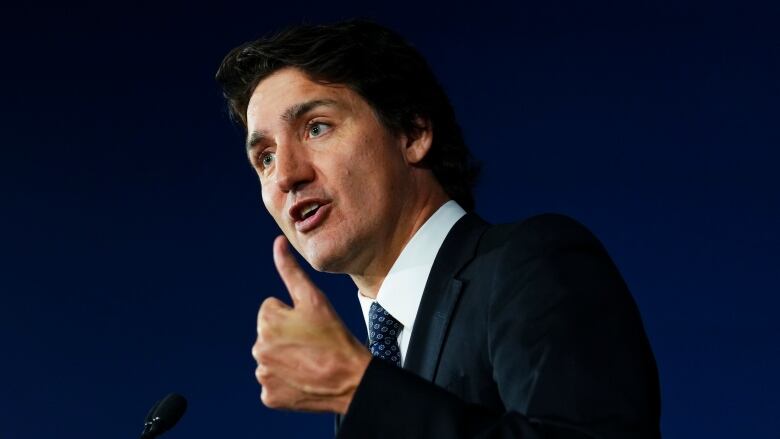 A man in a suit gestures while speaking into a microphone.