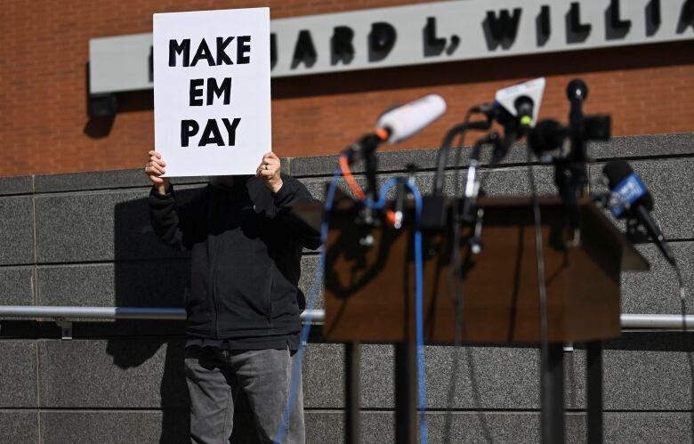 Man holds up sign that says: Make them pay.