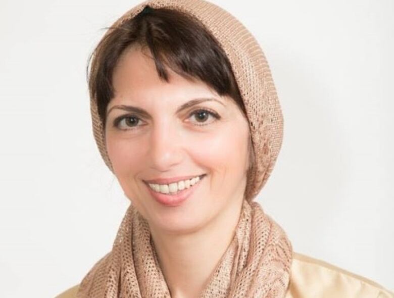 A woman with a beige scarf wrapped around her head and neck smiles.