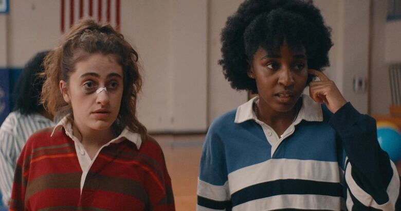 Two women wearing polo shirts give confused expressions. The woman on the left has a black eye and a bandage across her nose. 