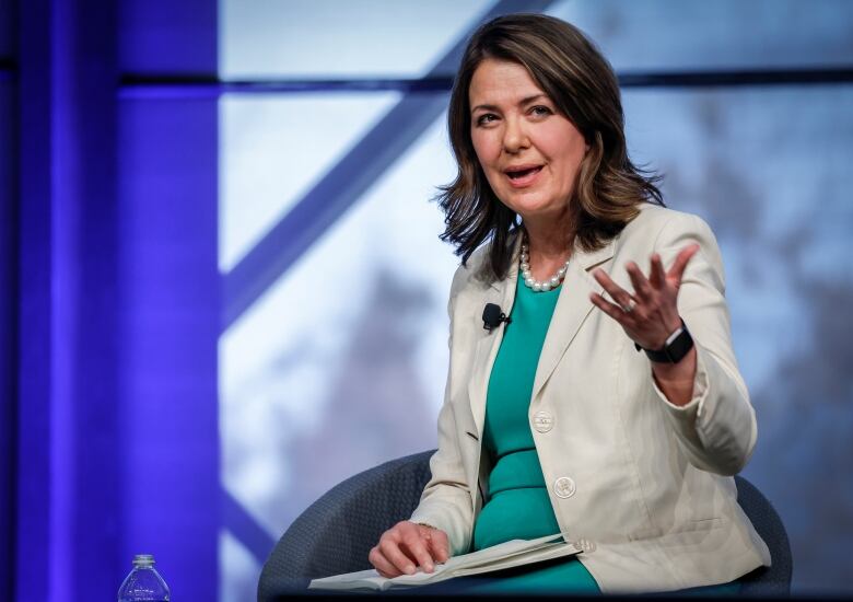 A woman raises her hand as she looks towards the camera.