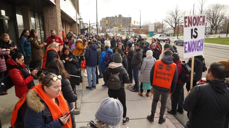 Striking public servants stand in front of a politician's office.