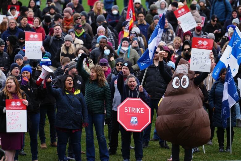 A crowd of striking public servants and supporters includes someone in a poop emoji costume.