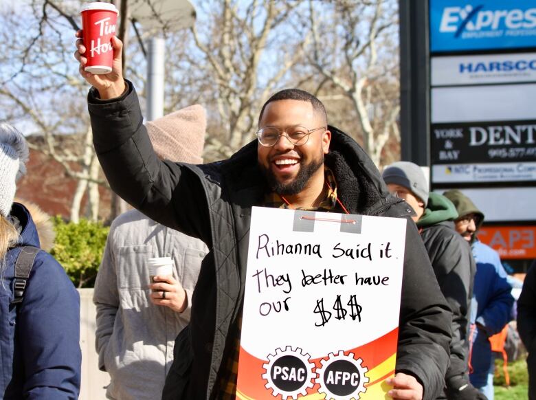 A man holding a sign that says Rihanna said it. They better have our $$$.