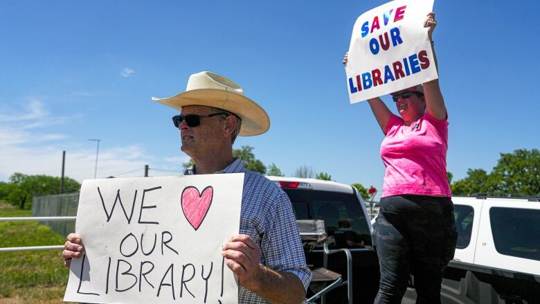 A man wearing a cowboy had holds a sign with the message 