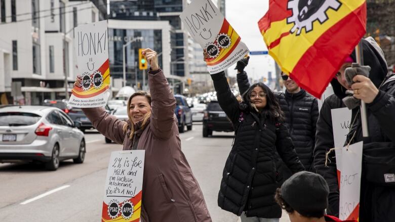 Two women hold signs asking drivers to 'honk' as they and others stand on a picket line in front of a taxation centre in Toronto.