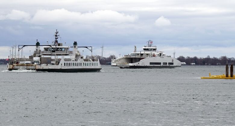 An older-looking, smaller ferry boat passes a long, sleek white boat. It's a grey, cloudy day and there are low waves on the water.