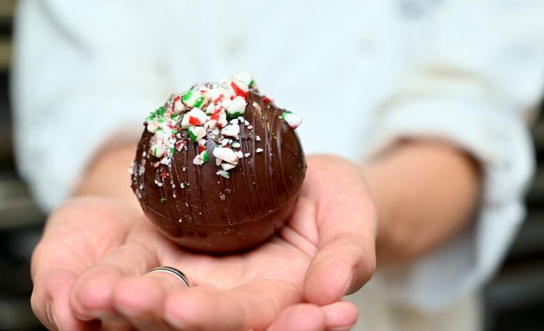 A closeup of hands holding a sphere of chocolate coated with bits of candy cane.