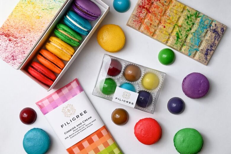 An overhead view of rainbow-coloured macarons, bonbons and a white chocolate bar that looks like it has been paint splattered. 