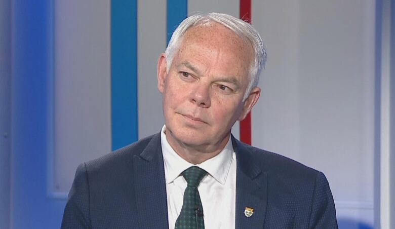 A white-haired man in a suit and tie sits in a television studio