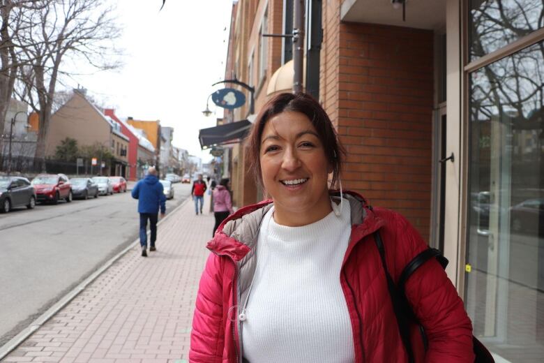 A woman in a pink coat looks at the camera, standing on a busy sidewalk