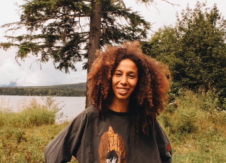 A woman in green shirt stands in front of a tree amid grasses.