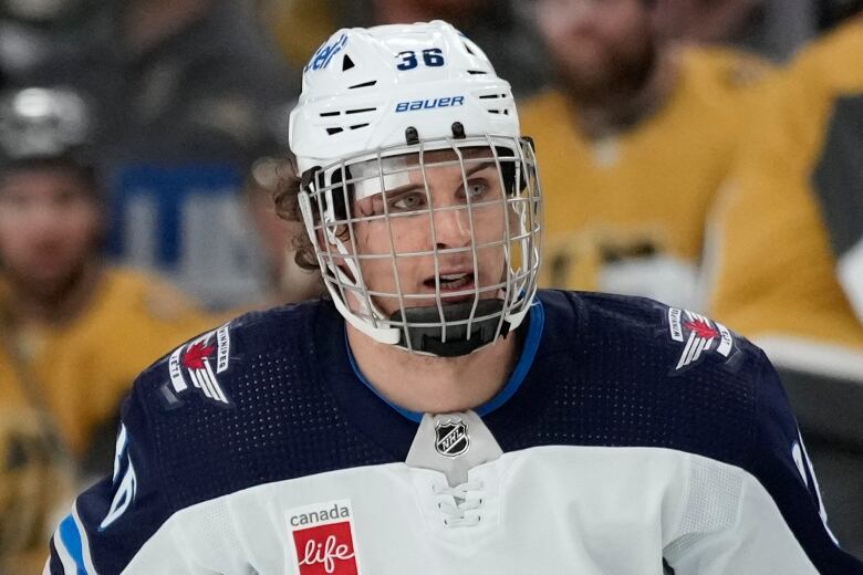 Jets player wearing a cage-style mask and a bandage on his right temple.