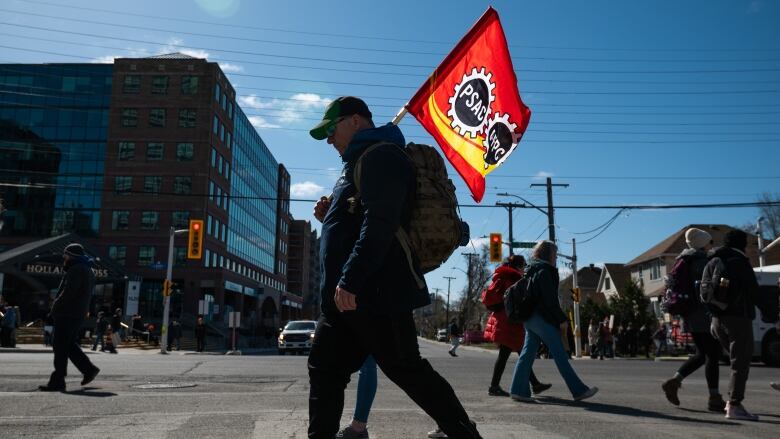 A striking worker carries a union flag across a crosswalk.