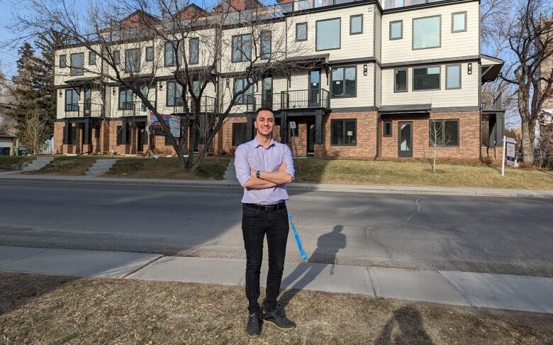 A man in his 20s stands in front of a stretch of row housing. 