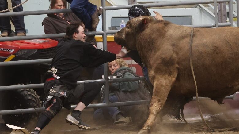 A man runs at a bull while someone else behind a fence, half-siting on the ground, watches.