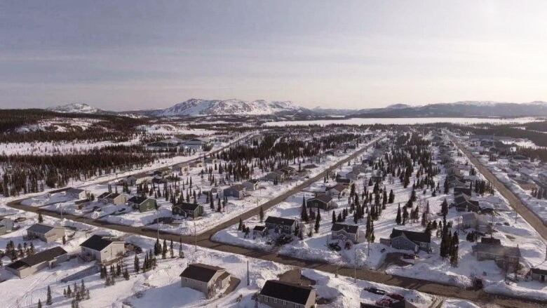 An aerial view shows Natuashish with rows of houses and mountains surrounding the community. 