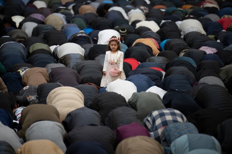 A toddler stands in the middle of a group of men kneeling and bent over during Eid al-Fitr prayers in Bucharest.