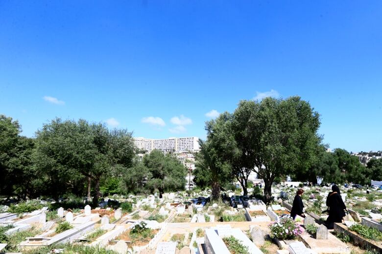 Two people walk by graves at a cemetery to pray at relatives' tombs, a tradition after Eid prayer.