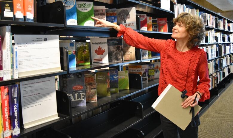 A woman points at a book on a shelf.