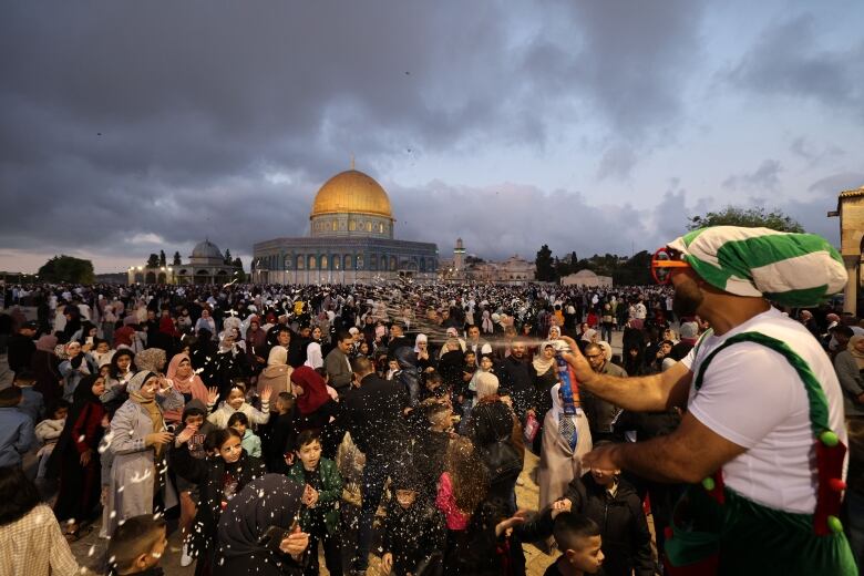 A man wearing jumbo red eyeglasses sprays a crowd of worshippers with foam, as part of Eid al-Fitr celebrations near the Dome of the Rock shrine.