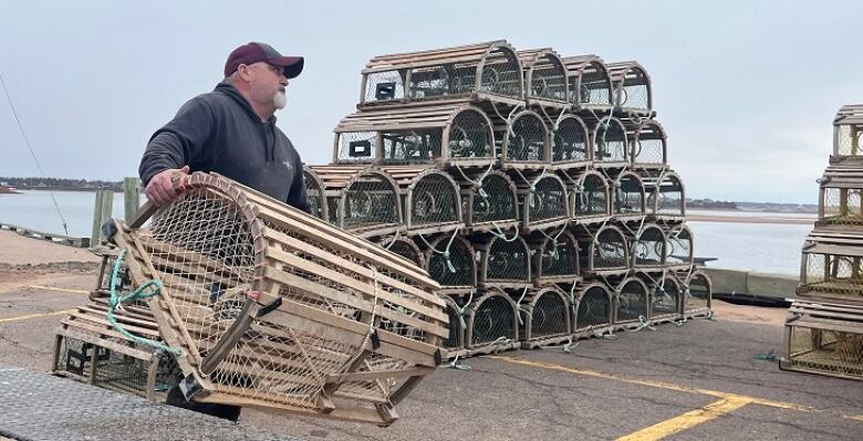 A man lifts a lobster trap off a truck to place it on a pile of traps in the background.