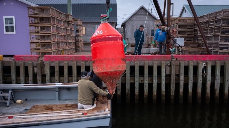 A crane lifts a large red buoy onto a fishing boat 