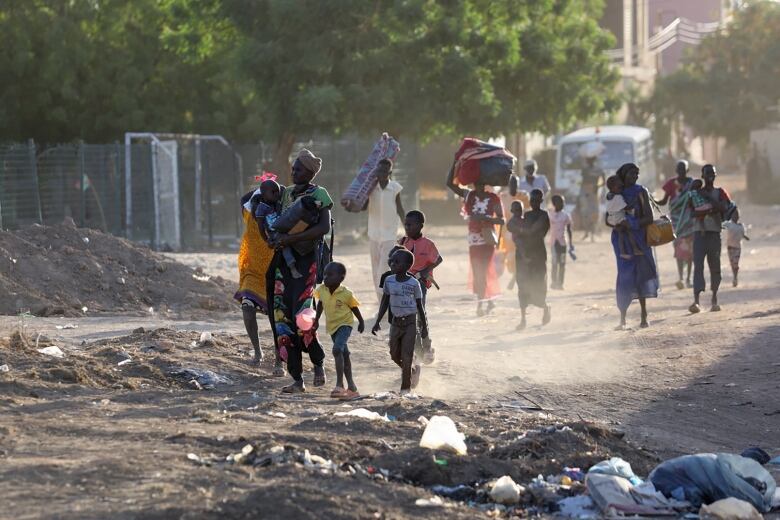 Women and children walk along a dirt road carrying belongings.