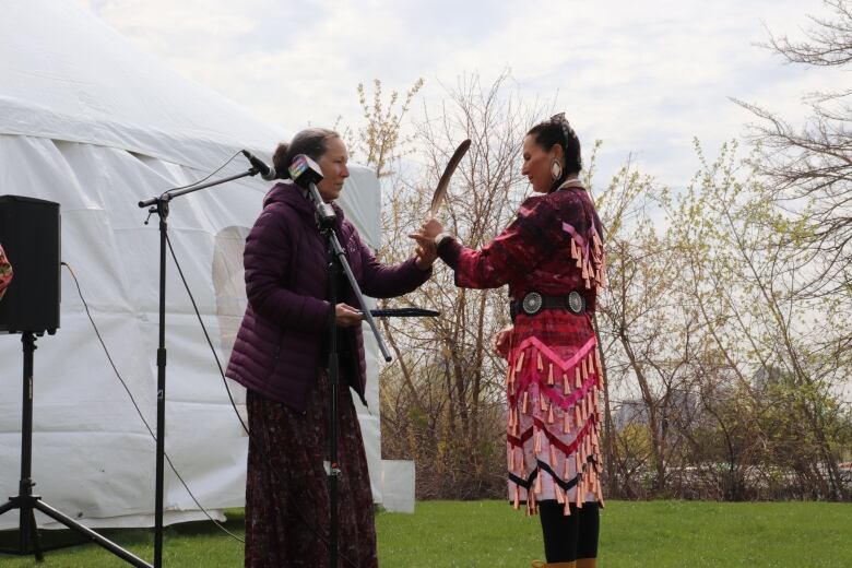 An Indigenous woman gives another Indigenous woman an eagle feather. 