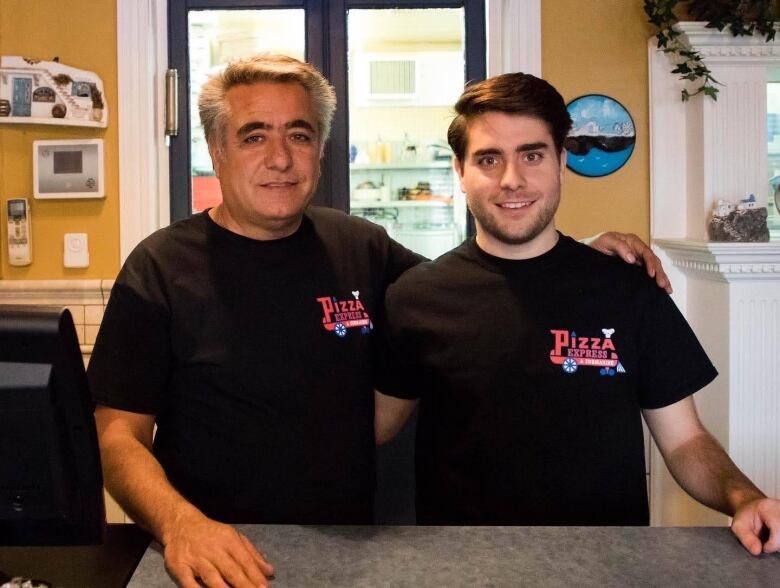 Two men stand smilling wearing black t-shirts.