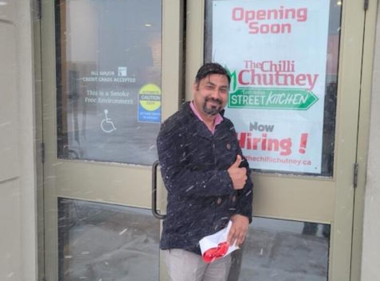 A man gives a thumbs up in front a sign announcing a restaurant opening.