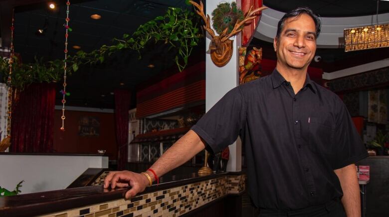 A man dressed in black stands smilling in an Indian restaurant.