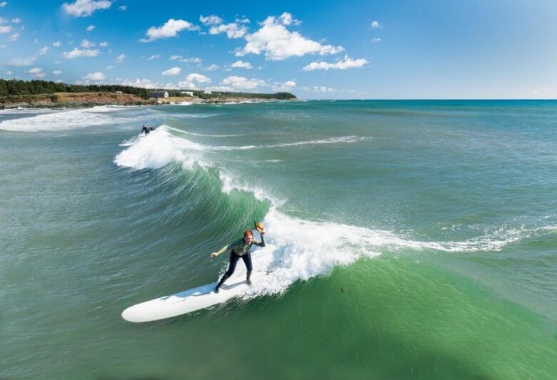 A woman surfs a wave in a blue and green ocean.