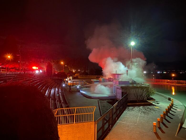 Flames and smoke are seen emerging from a small building at an amphitheatre, with a pool visible behind it.