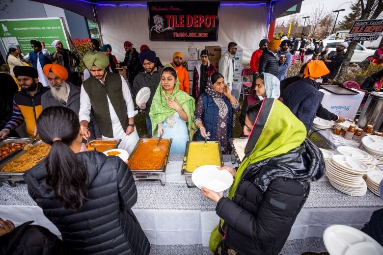 People at a tent line up with plates to eat food from heated trays. 