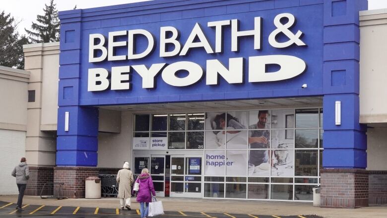 People walk in a parking lot toward a Bed Bath and Beyond store.