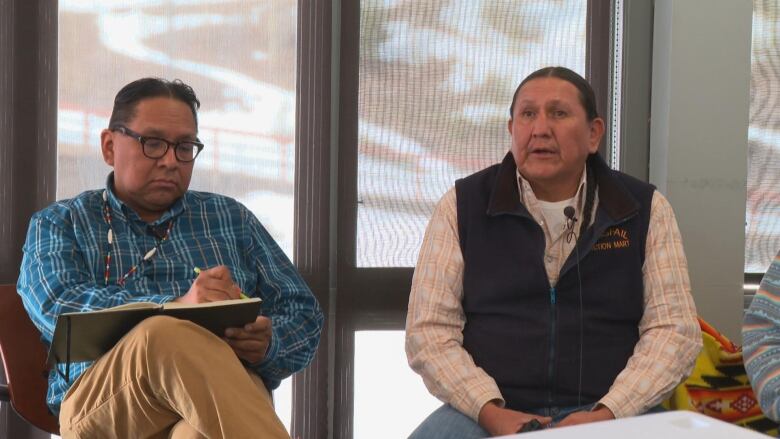 Two men are looking towards the camera while seated.