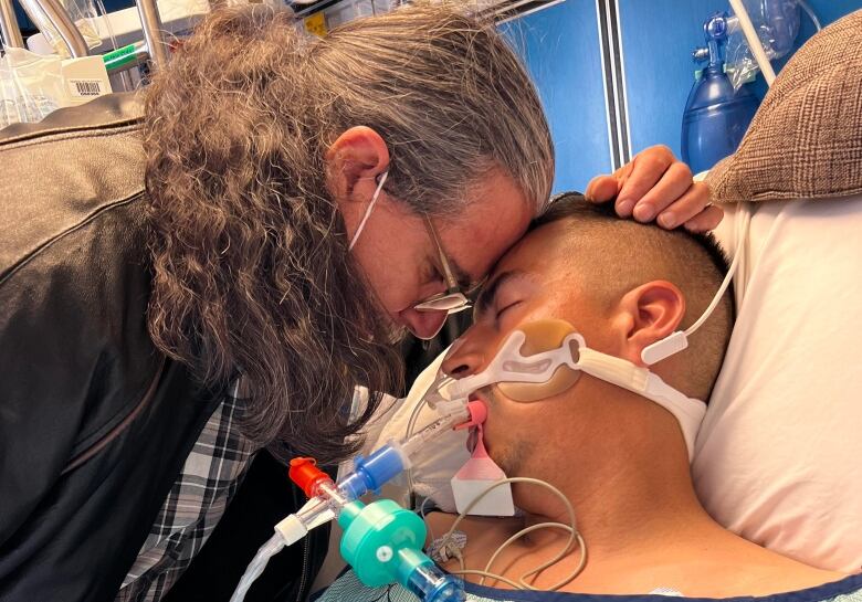 A father is pictured holding on to his son, who is on a ventilator.