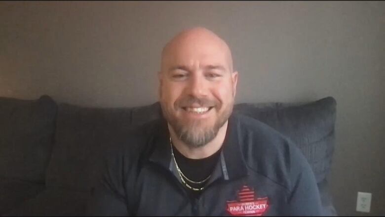 New Brunswick para hockey coach Shawn Lucas smiles during a zoom interview. He is wearing a black shirt with a red logo that says 'Para Hockey.'