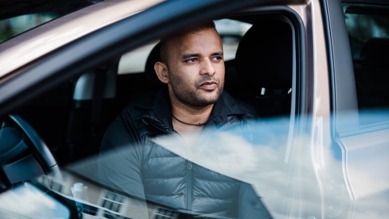 A man looks away from the camera while sitting in a car.