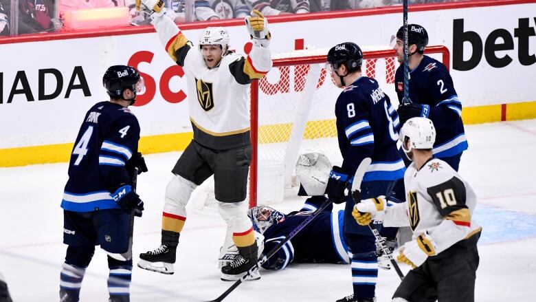 A hockey player celebrates scoring a goal with both of his arms up as three opposition players and a fallen goaltender are seen next to him.