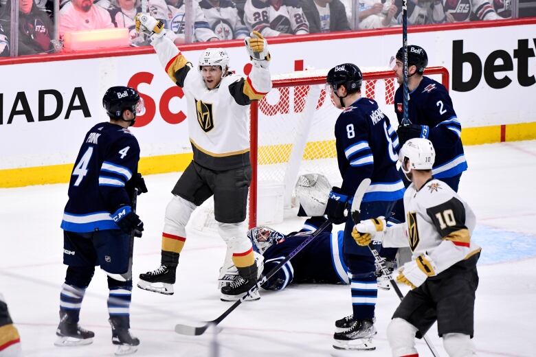 A hockey player celebrates scoring a goal with both of his arms up as three opposition players and a fallen goaltender are seen next to him.