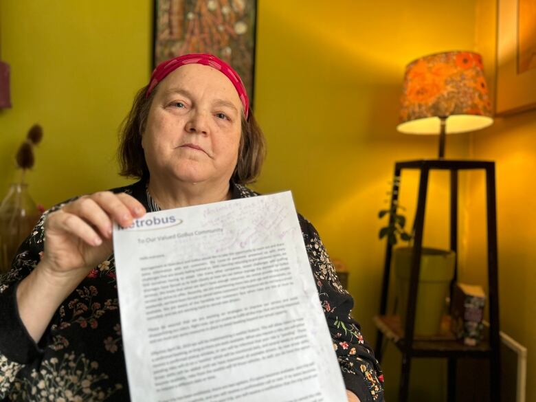 A woman wearing a pink headband and a shirt with a floral pattern holds a letter in front of the camera.