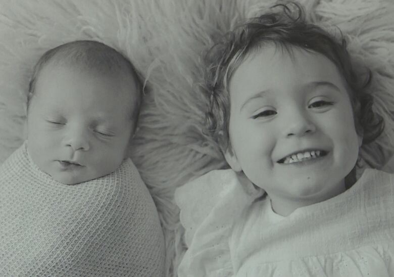 A newborn tightly wrapped on the left and a toddler, smiling, on the right.