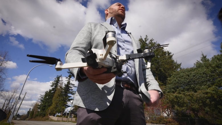 A man in a grey blazer holds a drone that is wrapped in black tape. 