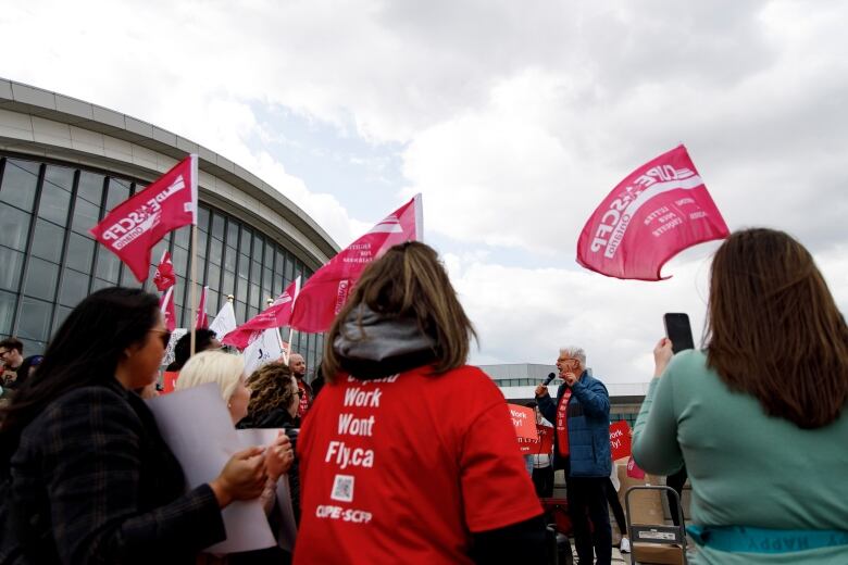 A white man speaks to a rally where people are waving pink flags.