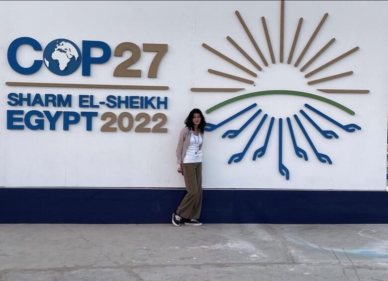 Woman stands in front of COP27 logo. 