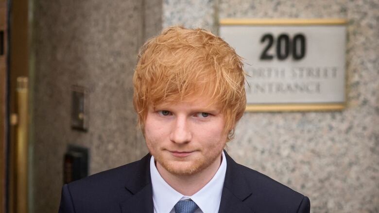 A man in a suit and tie is shown in closeup in a photograph taken outside a building.