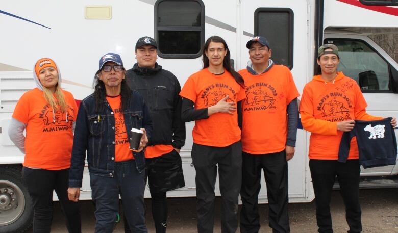 Six Indigenous people pose in front of their RV. 