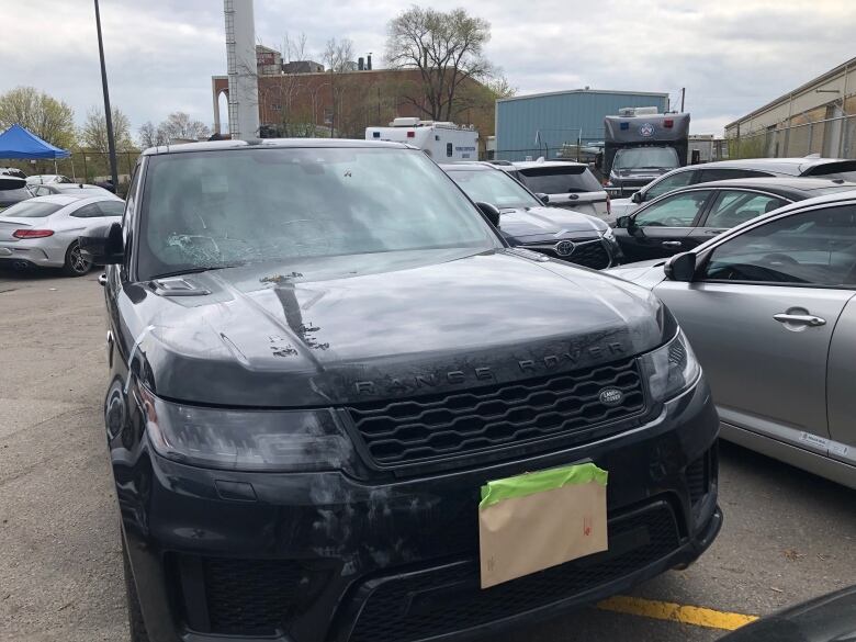 A black Range Rover in a parking lot. It has cracks in its front window. 